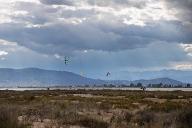 Denizde yağmurdan önce dramatik bulutları olan bir sürü uçurtma avcısı, Delta del Ebro 'daki Trabucador sahilinde uçurtmacılar.
