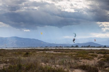 Denizde yağmurdan önce dramatik bulutları olan bir sürü uçurtma avcısı, Delta del Ebro 'daki Trabucador sahilinde uçurtmacılar.