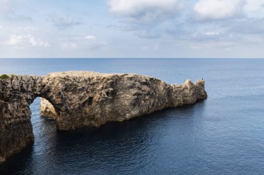 Ciutadella, Menorca 'da Pont d' en Gil, denizdeki kayadan köprü, burunda kemer, kayanın ucunda yalnız insan