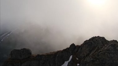 Dağların tepesinden gelen kalın bulutlar sisle örtülü, güneş bulutların arasından parlıyor. Sisli dağlar. Yüksek kalite 4k görüntü