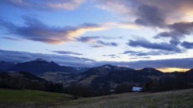  Tepe ve kırsal arazi, alacakaranlıkta hareket eden bulutlar, ağaçlarla kaplı çimenli çayırlar, karla kaplı dağlar. Kış ve bahar arasında bir uyanış cenneti. Yüksek kalite 4k görüntü