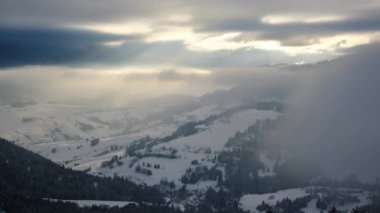 Zaman atlamalı sisli kış manzarası karla kaplı dağlar bulutlarla kaplı. Güneş ışınları bulutların arasında parlıyor. Yüksek kalite 4k görüntü