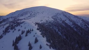 Kış batımında karlı bir dağın üzerinden uçmak, yukarıdan hava manzarası, Yüksek kalite 2K görüntü