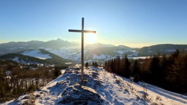 Kış doğasının manzarası, gündoğumunda karlı tepede çelik haçla kaplı, dindar Hıristiyan arka planı. Yüksek kaliteli FullHD görüntüler