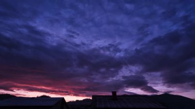 Güneş doğarken, evlerin çatılarının üstünde dramatik renkli bulutlar ve gökyüzü. Yüksek kalite 4k görüntü