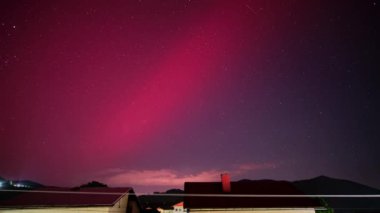 Evlerin siluetlerinin üzerinde kırmızı ve mor aurora, yıldızların yavaş çekimi, zaman ayarlı. Yüksek kalite 4k görüntü