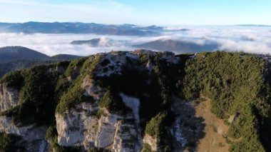 Ormanlı dağlık arazinin havadan görünüşü. Sis dolu bir vadi. Yoğun sis, sonbahar manzarasını sabah ışığında görkemli dağ zirvesinin altında kaplıyor. Yüksek kalite 4k görüntü