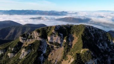 Ormanlı dağlık arazinin havadan görünüşü. Sis dolu bir vadi. Yoğun sis, sonbahar manzarasını sabah ışığında görkemli dağ zirvesinin altında kaplıyor. Yüksek kalite 4k görüntü