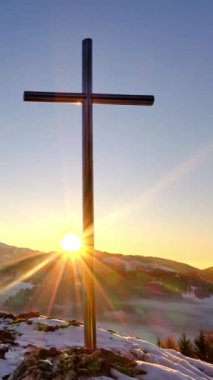 Vadide sisli, huzurlu, karlı ve sisli bir kış manzarasında Hristiyan haçı üzerinde renkli bir günbatımının dikey videosu. Sosyal medya için zaman aşımı.