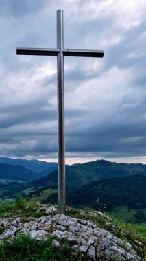 Zaman ayarlı bir video, yaz boyunca kayalık bir dağın zirvesinde duran metal bir haçı gösteriyor. Yavaşça sürüklenen bulutlar gökyüzünde hareket ederek dağlık bölgede sakin ve bulutlu bir hava yaratıyor..