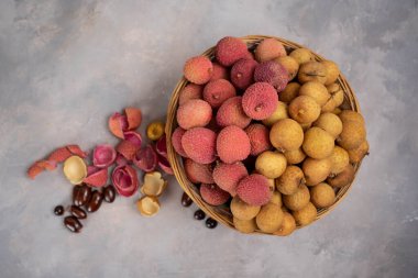 Lychee and longan in basket on gray stone background. Exotic fruits on tray at home. BIO fruits.