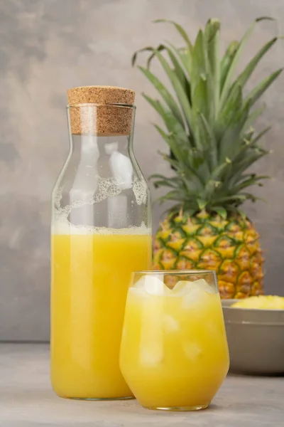 Pineapple juice in a clear glass and bottle on a light table. Pineapple and slices in the background. Pineapple fresh.