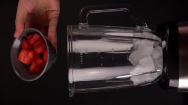 Transparent blender bowl filling with fresh sliced strawberry amd ice in slow motion close up. Making alchool coktail with blender.