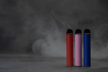 Çok renkli elektronik sigaralar koyu arka planda dumanla kaplanır. Yüksek kalite fotoğraf