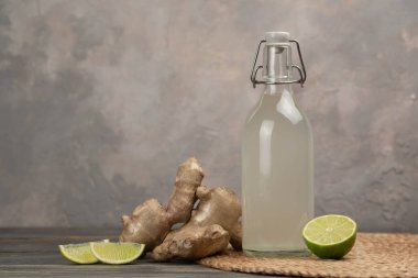 Gri arka planda ev yapımı zencefilli gazoz, limon ve zencefil kökü. Ön görünüm.