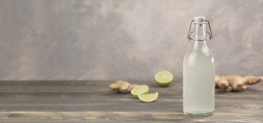 Gri arka planda ev yapımı zencefilli gazoz, limon ve zencefil kökü. Ön görünüm.