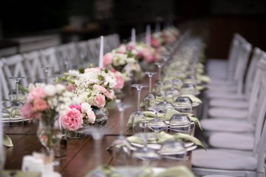 Büyük, uzun, süslü, ahşap bir masa örtüsü ve tabaklar, çiçekler, mumlar ile kaplı sandalyeler parkta, ormandaki yeşil çimlerin üzerinde duruyor. Düğün ziyafeti.