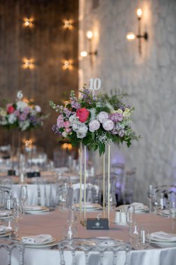 Masanın üzerinde yeşil yapraklar ve taze çiçeklerden yapılmış bir süs duruyor. Düğün günü. Taze çiçek süslemeleri. Şeftali ve beyaz takoz dekorasyonları.