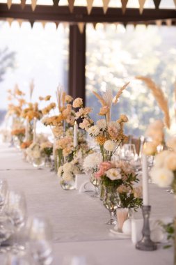 Büyük, uzun, süslü, ahşap bir masa örtüsü ve tabaklar, çiçekler, mumlar ile kaplı sandalyeler parkta, ormandaki yeşil çimlerin üzerinde duruyor. Düğün ziyafeti.