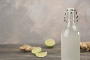 Gri arka planda ev yapımı zencefilli gazoz, limon ve zencefil kökü. Ön görünüm.