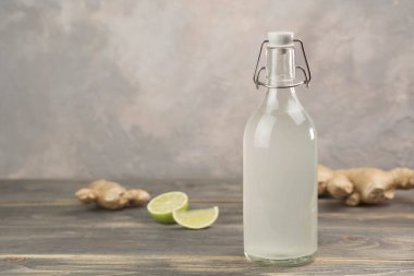 Gri arka planda ev yapımı zencefilli gazoz, limon ve zencefil kökü. Ön görünüm.