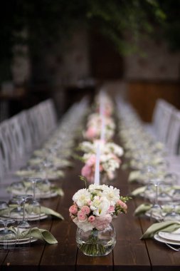 Büyük, uzun, süslü, ahşap bir masa örtüsü ve tabaklar, çiçekler, mumlar ile kaplı sandalyeler parkta, ormandaki yeşil çimlerin üzerinde duruyor. Düğün ziyafeti.