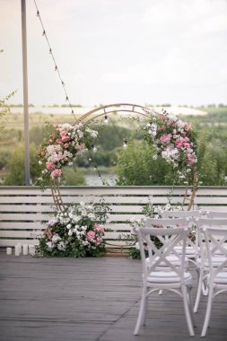 Güzel bir düğün hazırlığı. Düğün merasiminin alanı. Yuvarlak kemer, çiçeklerle süslenmiş beyaz sandalyeler, yeşillik. Sevimli, modaya uygun kırsal dekor. Festival dekorunun bir parçası, çiçek aranjmanı..