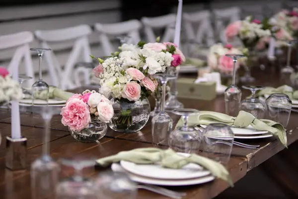 stock image A large, long, decorated, wooden table and chairs, covered with a white tablecloth with dishes, flowers, candles, stands on the green grass in the park, in the forest in nature. Wedding banquet.