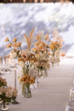 Büyük, uzun, süslü, ahşap bir masa örtüsü ve tabaklar, çiçekler, mumlar ile kaplı sandalyeler parkta, ormandaki yeşil çimlerin üzerinde duruyor. Düğün ziyafeti.