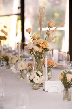 Büyük, uzun, süslü, ahşap bir masa örtüsü ve tabaklar, çiçekler, mumlar ile kaplı sandalyeler parkta, ormandaki yeşil çimlerin üzerinde duruyor. Düğün ziyafeti.