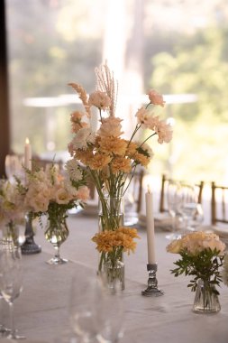 Büyük, uzun, süslü, ahşap bir masa örtüsü ve tabaklar, çiçekler, mumlar ile kaplı sandalyeler parkta, ormandaki yeşil çimlerin üzerinde duruyor. Düğün ziyafeti.