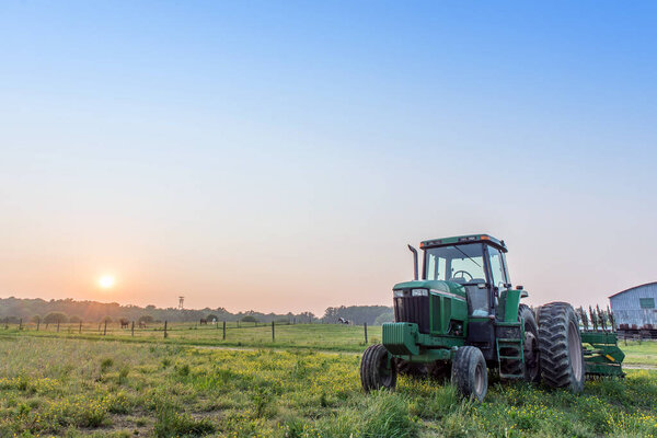 Agricultural landscape of a tractor in a field on a Maryland farm with the sun setting.