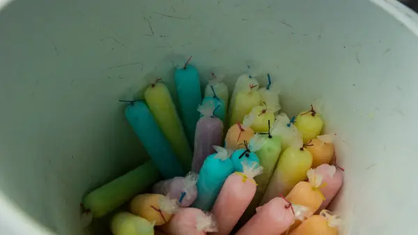 Renkli dondurulmuş şekerlerle dolu bir kova, çeşitli pastel gölgelerdeki buzlu şekerleri andırıyor. İkramlar plastiğe sarılmış, mavi, pembe, sarı ve yeşil renklerin karışımı sergileniyor..