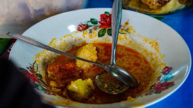 İçinde bir kaşık dolusu et ve patates bulunan baharatlı bir köri yemeğinin kalıntılarıyla dolu bir kase. Kasenin kenarında çiçek deseni var..