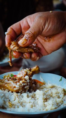 Bir parça tavuğu bir tabak pirincin üzerinde tutan bir el geleneksel yemekleri elleriyle sergiliyor..