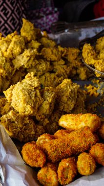 Altın çıtır tavuk parçaları ve portakallı kroketler de dahil olmak üzere çeşitli kızartma çeşitleri, dokulu arka planda bir tepside dizilmiş..
