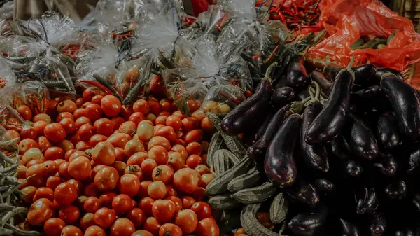 Canlı bir market tezgahında taze domates, patlıcan ve plastik torbalarda yeşil fasulyeler sergileniyor..
