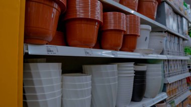 Bir mağazanın raflarında çeşitli saksıların sergilendiği bir sergi. Tencerelerin farklı renkleri ve boyutları var. Terracotta, beyaz ve siyah da dahil. Raflar iyi düzenlenmiş, ürünleri çekici bir şekilde sergiliyorlar..