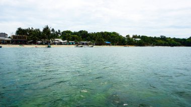 Deniz kenarındaki sakin bir tropikal köyün sakin manzarası yemyeşil ağaçlar, antika evler ve sakin okyanus dalgaları bir rahatlama ve doğal güzellik hissi veriyor.