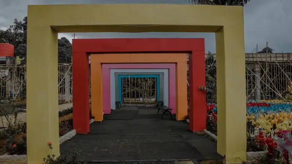 Bahçede renkli geometrik kemerler, banklar ve çiçeklerle.