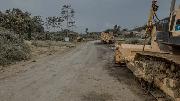 Ağaçlarla çevrili toprak bir yolda ağır makineleri olan bir inşaat alanı..