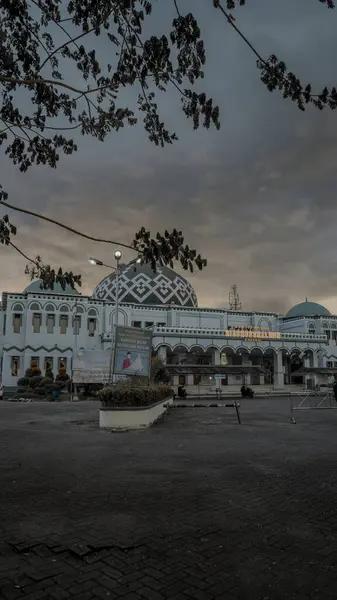 Ağaçlar ve bulutlu bir gökyüzü ile çevrili, karmaşık tasarımları olan bir caminin güzel mimari manzarası. Sahne, oranın sakin atmosferini yakalar.