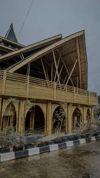 Karmaşık mimari tasarımı olan eşsiz bir bambu cami yapısı, eğimli çatılar ve kemerli girişler, bulutlu bir gökyüzüne karşı kurulmuş..