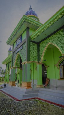 Karmaşık mimari detayları ve mavi kubbesi olan canlı yeşil bir cami..