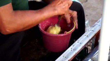 Metal bir bankta oturan, kırmızı plastik bir kovaya hamur karıştıran bir adam..