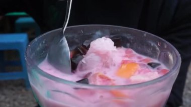 İçi buz küpleri ve siyah jöle parçalarıyla dolu pembe tatlı içeceğiyle dolu bir bardağın yakın plan çekimi. İçindekileri karıştıran bir kaşıkla..