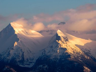 Kışın dağların manzarası. Tatra Ulusal Parkı - Czarna Gora 'dan. Dağ zirveleri, bulutların arasından parlayan batan güneşin ışınlarıyla aydınlanır. Spisz. Malopolskie. Polonya.