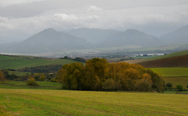 Горный пейзаж. На переднем плане сельхозугодия и осенние деревья. Вдалеке можно увидеть регион Низкие Татры Жилина. Liptovske Matiasovce. Словакия.