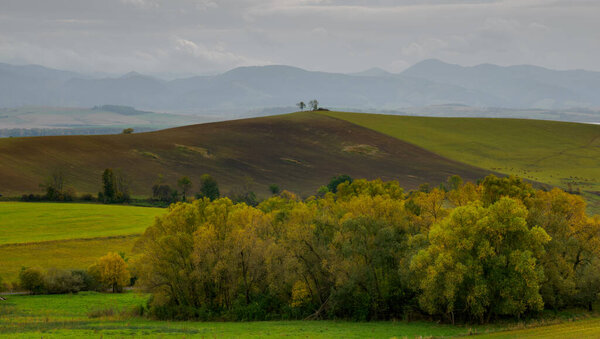 Mountain landscape. In the foreground, a farmland and autumn trees. In the distance you can see the Low Tatras Zilina Region. Liptovske Matiasovce. Slovakia.