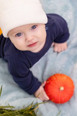 Puff ball şapkalı şirin bir kız çocuğu parkta yerde oturmuş, elinde bir balkabağı, gülümsüyor ve oynuyor. Mutlu çocukluk kavramı. Kameraya bakıyorum. Yüksek kalite fotoğraf
